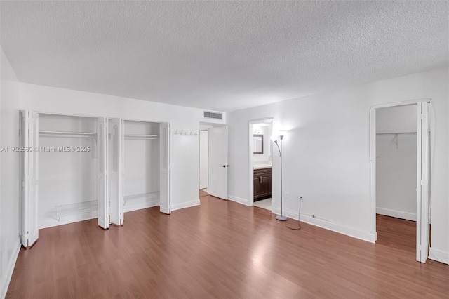 unfurnished bedroom with wood-type flooring, connected bathroom, a textured ceiling, and two closets