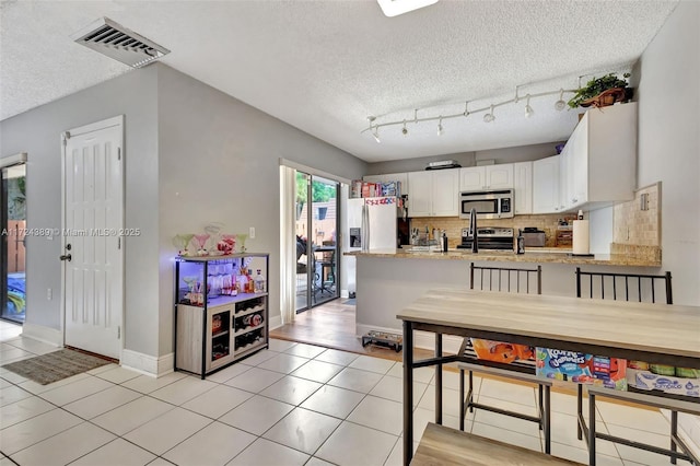 kitchen with stainless steel appliances, white cabinets, a textured ceiling, decorative backsplash, and light tile patterned flooring