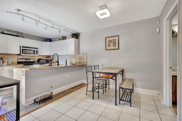 kitchen featuring white cabinets, decorative backsplash, light stone counters, and appliances with stainless steel finishes