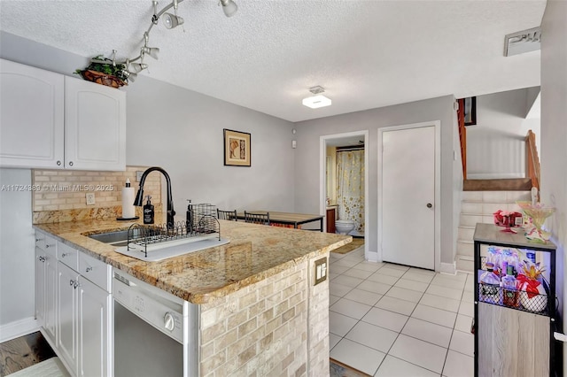 kitchen with white cabinets, sink, stainless steel dishwasher, light tile patterned floors, and light stone counters