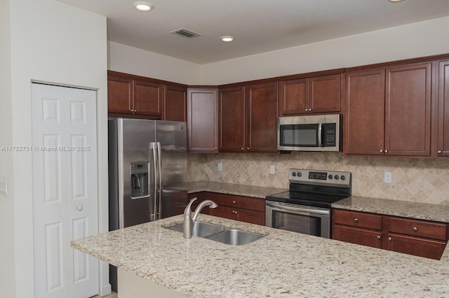 kitchen featuring decorative backsplash, light stone counters, sink, and appliances with stainless steel finishes