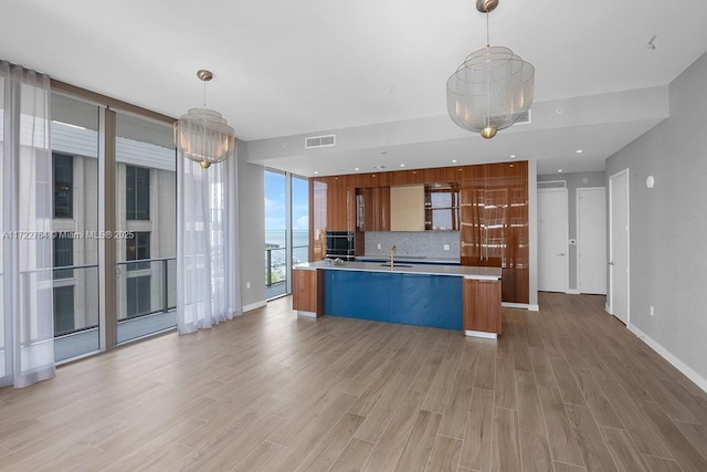 kitchen with pendant lighting, sink, light hardwood / wood-style flooring, a kitchen island with sink, and tasteful backsplash