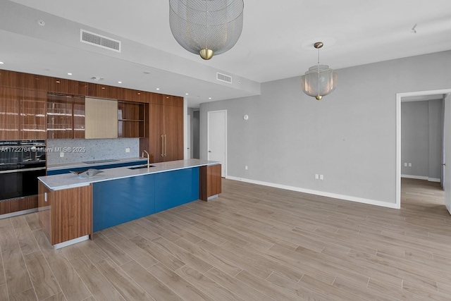 kitchen featuring tasteful backsplash, a center island with sink, light hardwood / wood-style floors, and black appliances