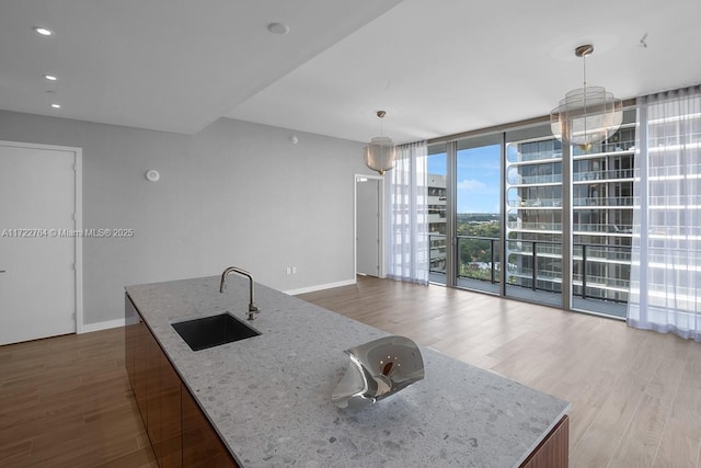 kitchen featuring floor to ceiling windows, sink, hanging light fixtures, a center island with sink, and light hardwood / wood-style floors