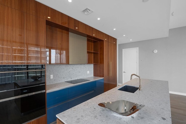 kitchen with a kitchen island with sink, sink, light stone countertops, and black electric cooktop