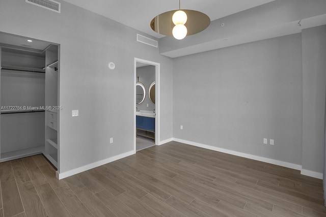 unfurnished bedroom featuring connected bathroom, hardwood / wood-style floors, a spacious closet, ceiling fan, and a closet