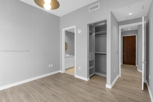 unfurnished bedroom featuring connected bathroom, a spacious closet, light hardwood / wood-style flooring, and a closet