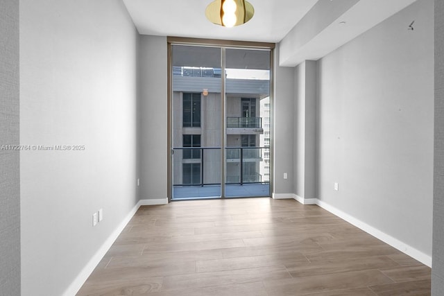 unfurnished room with a wall of windows and light hardwood / wood-style floors