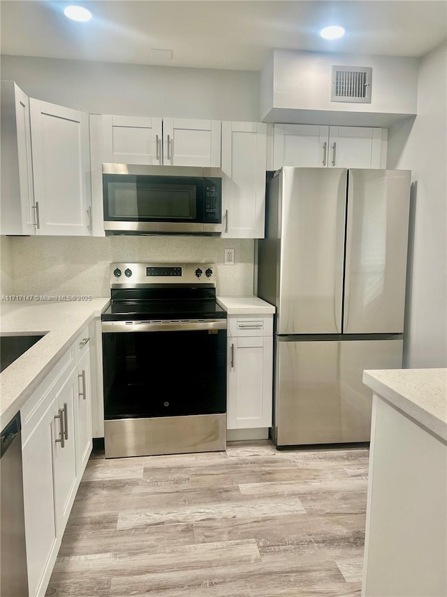 kitchen featuring white cabinets, backsplash, stainless steel appliances, and light hardwood / wood-style flooring