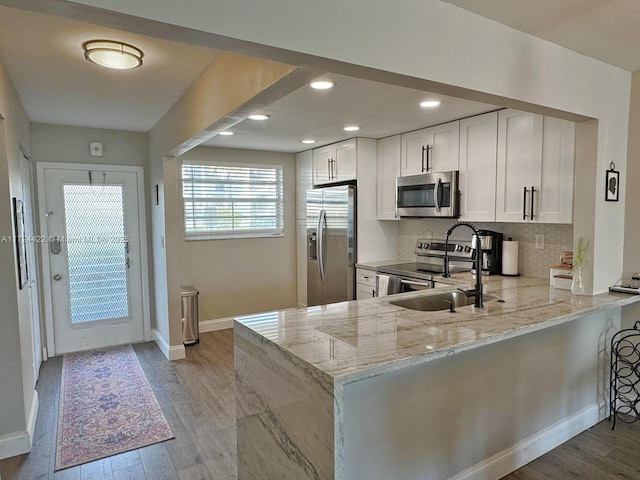 kitchen featuring kitchen peninsula, appliances with stainless steel finishes, tasteful backsplash, light stone counters, and white cabinets