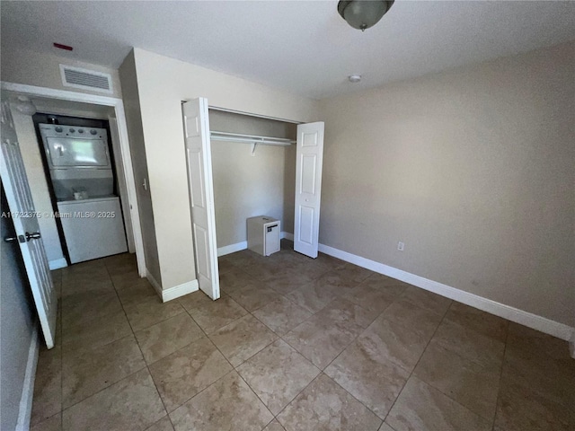 unfurnished bedroom featuring tile patterned flooring, stacked washing maching and dryer, and a closet