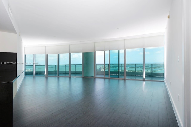 unfurnished room with plenty of natural light, a wall of windows, and dark wood-type flooring