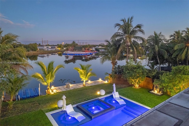 pool at dusk with a lawn, an in ground hot tub, and a water view