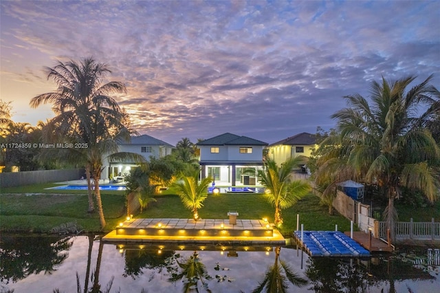 back house at dusk with a water view, a fenced in pool, and a yard