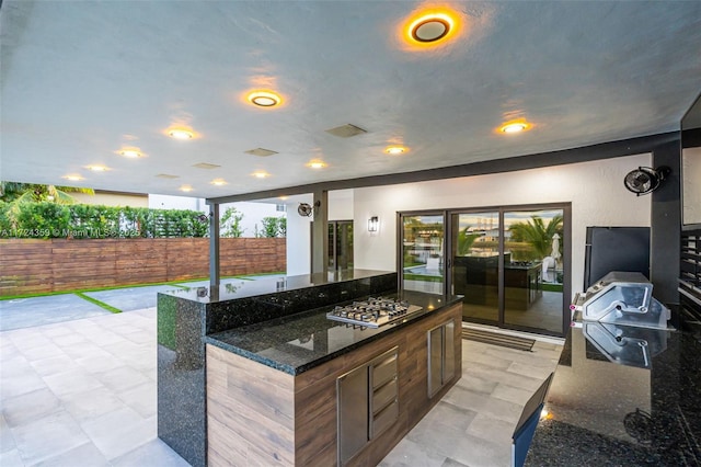 kitchen featuring stainless steel gas stovetop, an island with sink, and dark stone counters