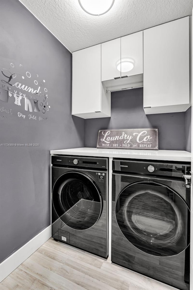 laundry room with washer and dryer, cabinets, light wood-type flooring, and a textured ceiling