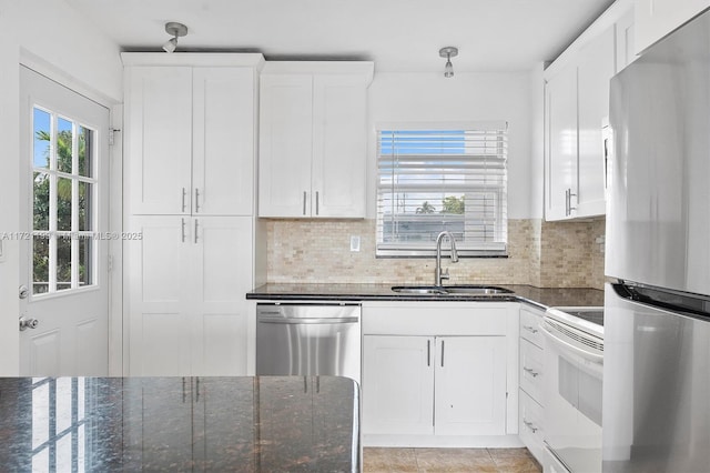 kitchen with sink, appliances with stainless steel finishes, white cabinetry, dark stone countertops, and decorative backsplash