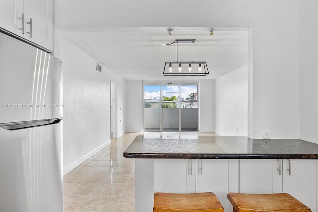 kitchen featuring pendant lighting, a breakfast bar area, stainless steel fridge, white cabinetry, and kitchen peninsula