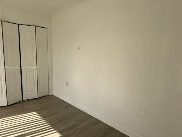 unfurnished bedroom with a textured ceiling, a closet, and dark wood-type flooring