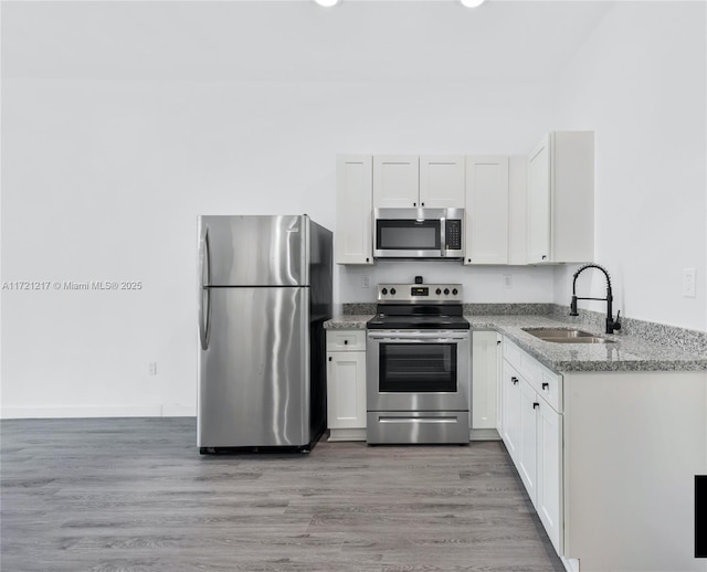 kitchen featuring appliances with stainless steel finishes, light stone counters, sink, hardwood / wood-style flooring, and white cabinetry