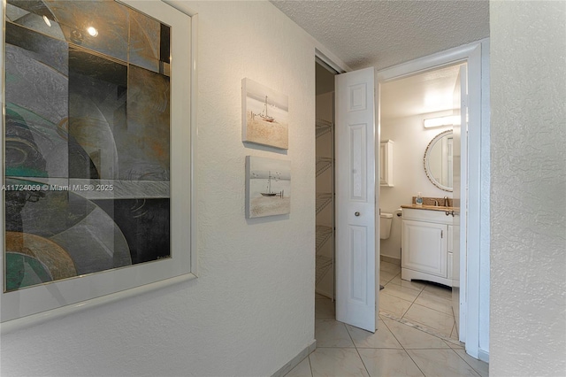 hall with sink, light tile patterned flooring, and a textured ceiling