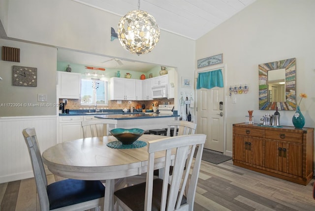 dining space featuring vaulted ceiling, light wood finished floors, wainscoting, and a chandelier