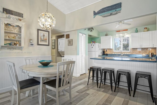 dining room with a wainscoted wall, stacked washer and dryer, visible vents, a decorative wall, and ceiling fan with notable chandelier