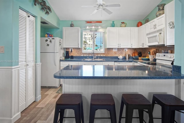 kitchen with white appliances, white cabinets, light wood-style flooring, a breakfast bar, and a sink