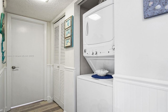 laundry area with a wainscoted wall, laundry area, a textured ceiling, and stacked washer and clothes dryer