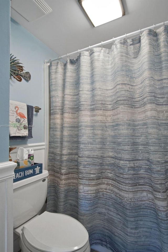 full bath featuring a shower with shower curtain, wainscoting, visible vents, and toilet