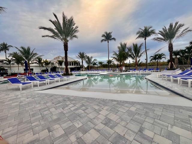 pool at dusk featuring a patio, fence, and a community pool