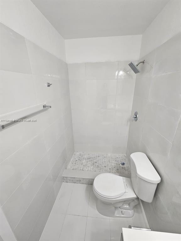 bathroom with tile walls, toilet, tiled shower, and tile patterned flooring