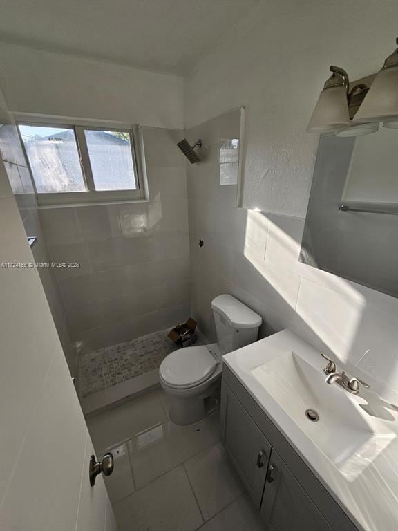 bathroom with toilet, vanity, tile patterned floors, and a tile shower