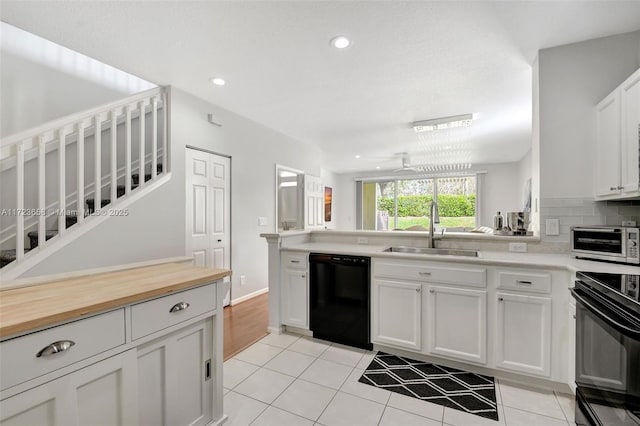 kitchen featuring light tile patterned floors, white cabinetry, ceiling fan, black appliances, and sink