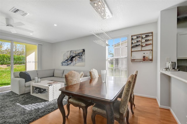 dining room with a healthy amount of sunlight, light wood-type flooring, and ceiling fan with notable chandelier