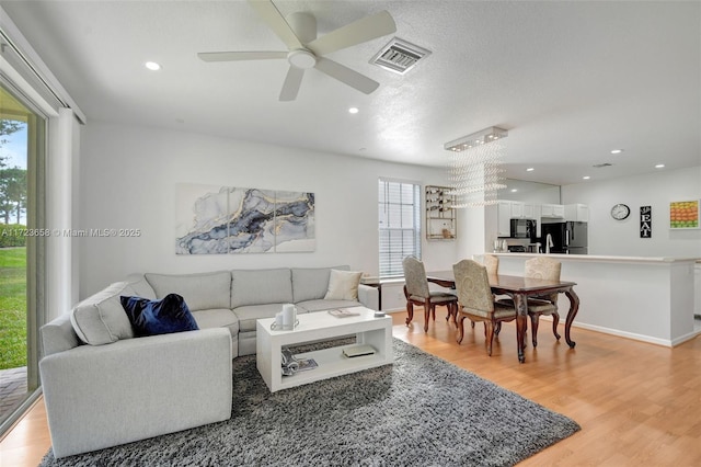 living room featuring light wood-type flooring and ceiling fan with notable chandelier