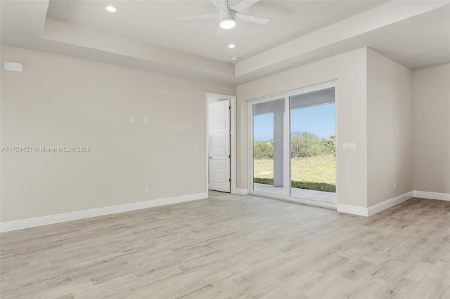 spare room with ceiling fan, a tray ceiling, and light hardwood / wood-style floors