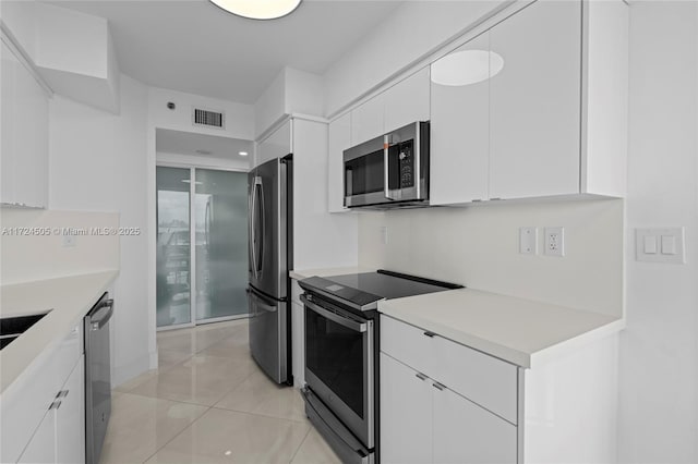 kitchen with stainless steel appliances, white cabinetry, and light tile patterned flooring