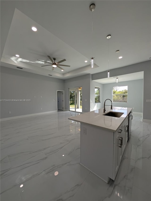 kitchen with pendant lighting, a raised ceiling, sink, ceiling fan, and an island with sink