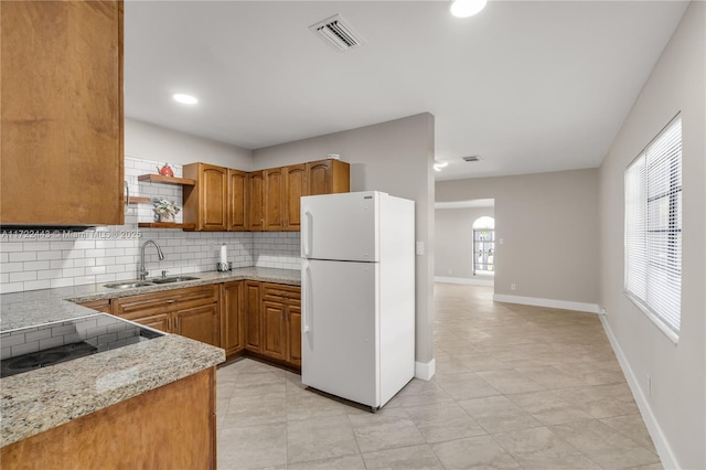 kitchen with white refrigerator, sink, light stone countertops, light tile patterned floors, and tasteful backsplash