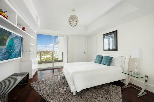 bedroom featuring a raised ceiling, dark wood-type flooring, and access to outside