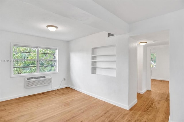 unfurnished room featuring wood-type flooring, built in shelves, and a wall mounted AC