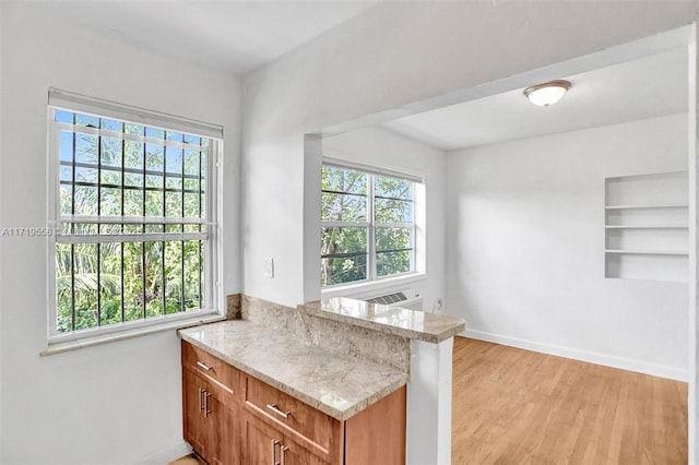 kitchen with kitchen peninsula, a wealth of natural light, light stone counters, and light hardwood / wood-style flooring