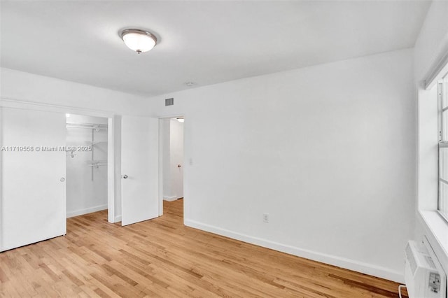 unfurnished bedroom featuring a wall mounted air conditioner, a closet, and light wood-type flooring