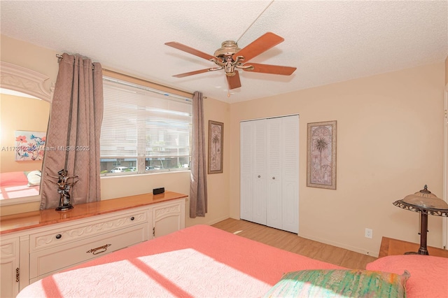 bedroom with ceiling fan, a closet, light hardwood / wood-style floors, and a textured ceiling