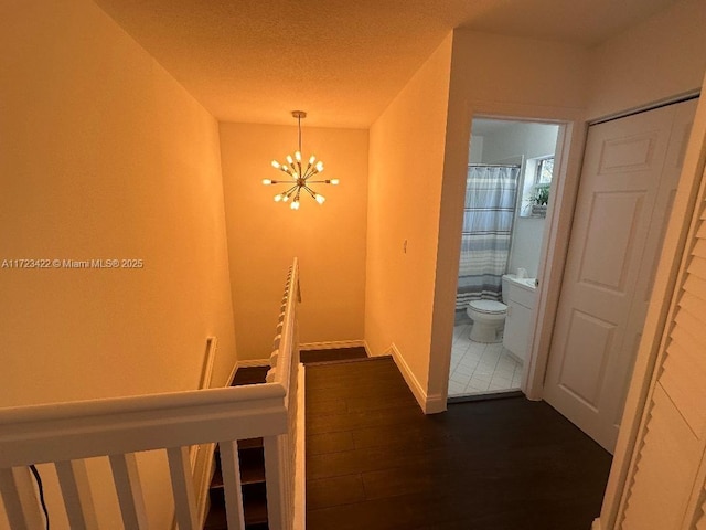 hallway featuring dark wood-type flooring, a textured ceiling, and a notable chandelier