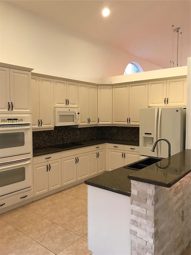 kitchen with sink, dark stone countertops, pendant lighting, white appliances, and light tile patterned floors