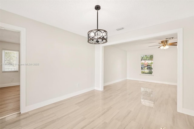 empty room featuring ceiling fan with notable chandelier and a textured ceiling