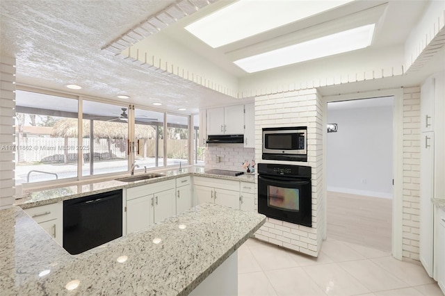 kitchen featuring white cabinetry, light tile patterned flooring, black appliances, and light stone counters