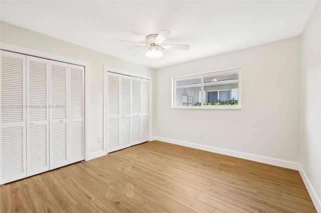 unfurnished bedroom featuring light hardwood / wood-style flooring, ceiling fan, and multiple closets